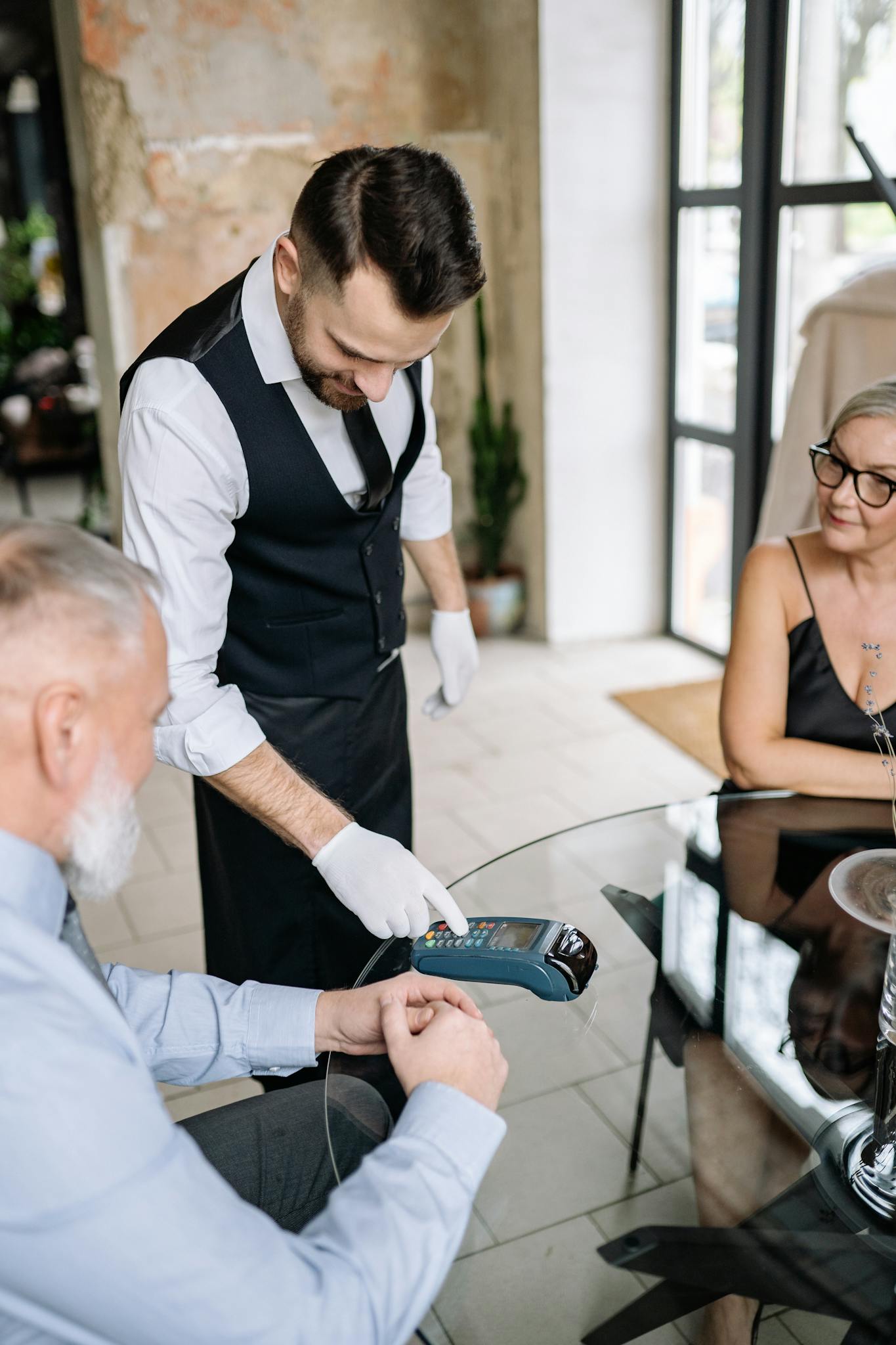 Senior couple paying with card at a restaurant, assisted by a waiter using a terminal.